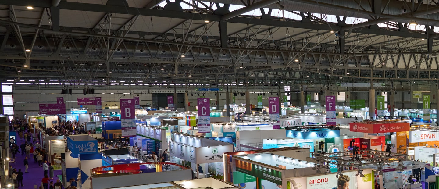 A trade fair hall seen from above, aisles of booths and visitors at a distance