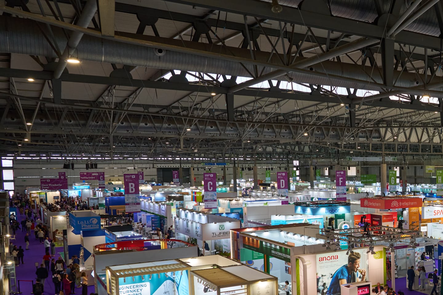 A trade fair hall seen from above, a field of booths under the roof trusses