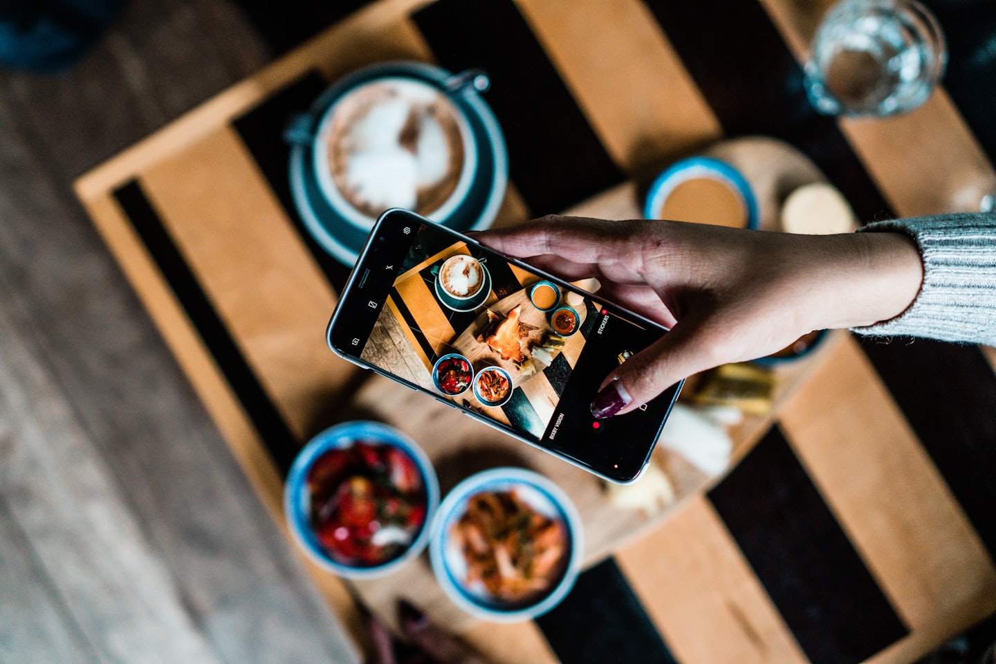 Overhead view of a hand framing a table of food and coffee on a phone screen