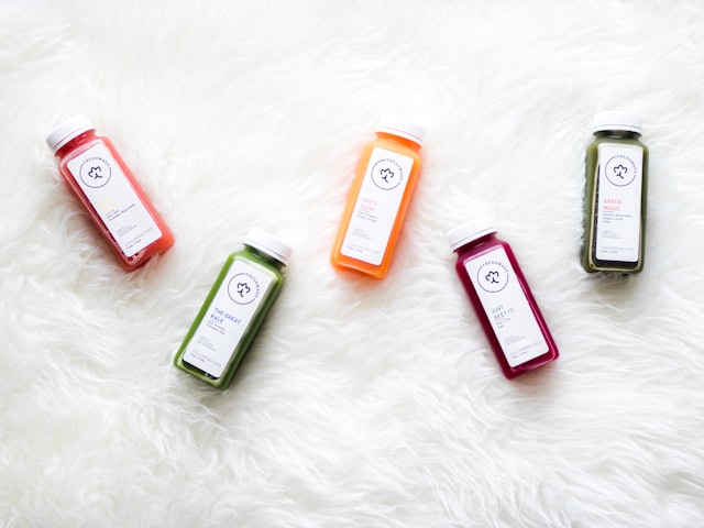 Five small juice bottles in bright colors on soft white ground